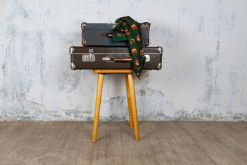 Vintage retro suitcase, the suitcase and there is a scarf on it, stand on a stool. The background is a white wall. The concept of retro travel and retro design.