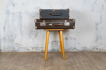 Two vintage suitcases stand on a stool against a white wall. The concept of retro travel and retro...