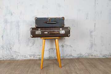 Two vintage suitcases stand on a stool against a white wall. The concept of retro travel and retro design.