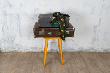 Vintage retro suitcase, the suitcase and there is a scarf on it, stand on a stool. The background is a white wall. The concept of retro travel and retro design.