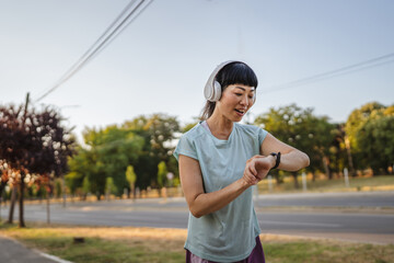 Happy japanese woman runner with headphones checking smart watch