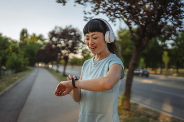 Happy japanese woman runner with headphones checking smart watch