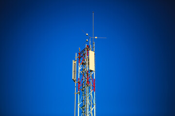 Telecommunication tower with antennas and signal equipment against a vibrant clear blue sky. Ideal...