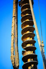 Fototapete Vertical view of a large industrial auger drill used in construction and earth drilling. The image captures the full length of the spiral drill bit with surrounding cables © dizain