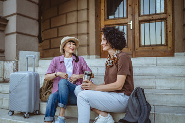 two women tourist friends with suitcases discuss on staircase