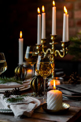 Beautiful table setting for family Christmas dinner at home. Cozy atmosphere, candlelight. Wine glasses, vintage chandelier, elegant interior. Fir tree branches, wooden furniture, dark, bokeh