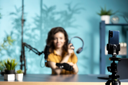 Focus on cellphone used by content creator in studio filming wireless headphones review for online streaming platforms. Close up of mobile phone recording media star comparing music listening devices