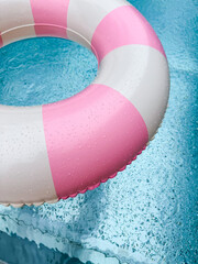 Swimming ring with pink and white stripes in a blue outdoor pool. Poolside atmosphere. Pink float.