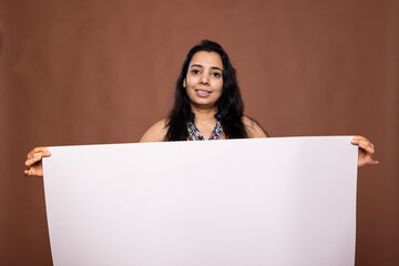 Indian woman stands holding blank white banner, ready for advertisement use against brown...