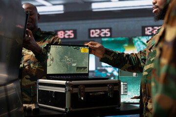 Military officer conducts tactical reconnaissance in command room, utilizing laptop for data...