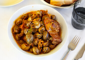 Appetizing stewed snails served on plate with rabbit meat and sausages