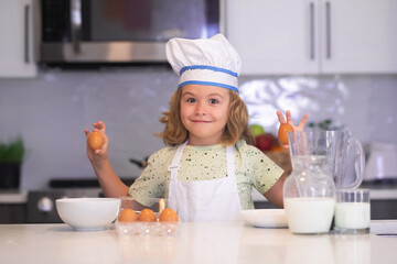 Funny kid with eggs at kitchen. Child chef cook. Funny child stand at kitchen table have fun baking, doing bakery preparing food at home kithen. Healthy food. Little chef preparing healthy meal.