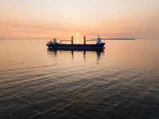 Breathtaking drone view of a cargo ship silhouette on the open sea against an epic orange sunset.