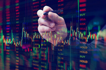 A close-up of a hand with a stylus interacting with a digital stock market chart. The overlay of candlestick graphs, buy and sell signals and numerical data.