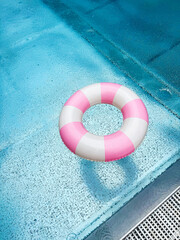 Swimming ring with pink and white stripes in a blue outdoor pool. Poolside atmosphere. Pink float.