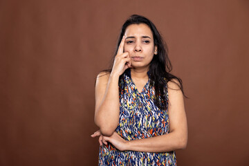 Attractive indian woman stands with a focused gaze, lightly pressing index fingers to her temples...