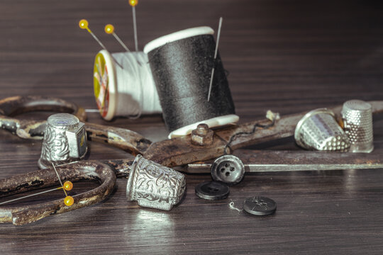 Silver sewing needles, Thimbles, Steel scissors, Measuring tape, Black buttons, Spools of black and white thread including pins on wooden blackground. Sewing items, Sewing notions, Sewing objects.