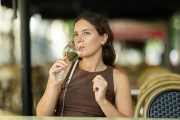 Young woman is sitting on the terrace of a cafe with a glass of white vein. European woman after a walk went to a restaurant and tastes wine