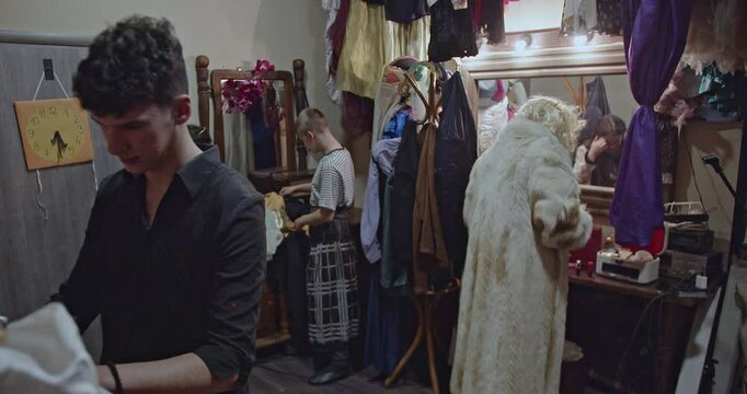Actors prepare backstage in a dressing room, trying on costumes and makeup before a theater play.