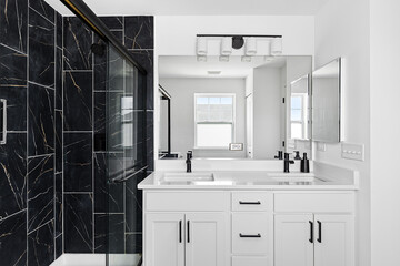 A bathroom with a white cabinet, black faucets on a quartz countertop, and black tiled shower.