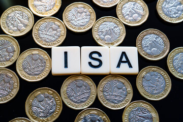 Individual Savings Account. Flat-lay of ISA letter tiles encircled by multiple British pound coins signifying UK tax-efficient personal savings.