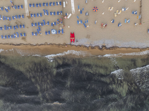 Aerial view of the sandy beach dotted with blue sunbeds meeting the clear turquoise water, creating a serene coastal scene., Santa Maria di Castellabate, Salerno, Italy.
