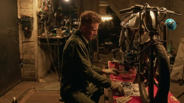 Young mechanic referencing blueprint while repairing vintage motorcycle in his dimly lit basement workshop
