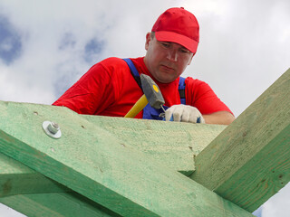 Carpenter driving a nail into house rafter beam