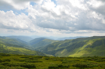 Beautiful green mountains ans hills with a mix of grasslands and shrubs spread across the horizon beneath a partly cloudy sky, embodying serenity and natural beauty. Svydovets, Carpathians, Ukraine