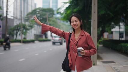 Professional woman hailing taxi, gripping takeaway coffee against urban backdrop