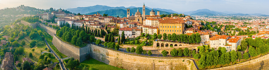 Aerial view of Bergamo&rsquo;s Citt&agrave; Alta in Italy with terracotta rooftops, historic churches, and mountain backdrop on a clear day