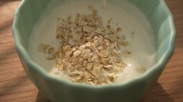 Oats falling into creamy yogurt in a green ceramic bowl