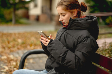 Sweet Girl Scrolling Phone While Sitting On Bench Outside