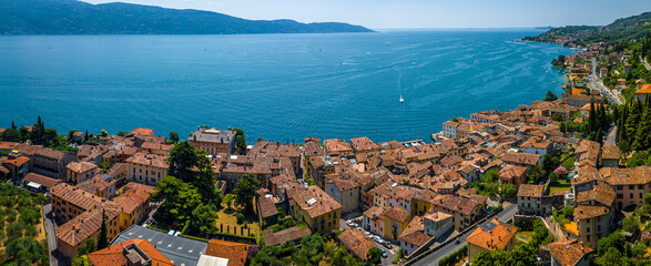 Aerial view of a pink historic church with bell tower in Gargnano, Lake Garda, Italy, surrounded by mountains and blue lake waters.