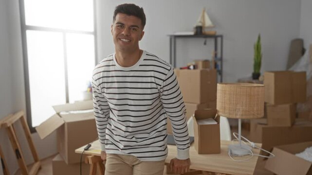 Young man in striped shirt smiling in a bright room with boxes, suggesting a new home setting, emphasizing a fresh start and positive atmosphere.