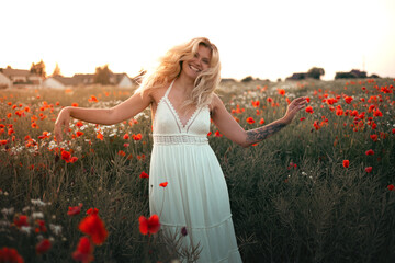 young beautiful blonde woman in white dress in poppy field at sunset. Woman and nature