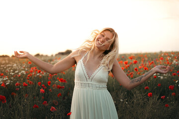 young beautiful blonde woman in white dress in poppy field at sunset. Woman and nature