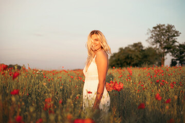 young beautiful blonde woman in white dress in poppy field at sunset. Woman and nature