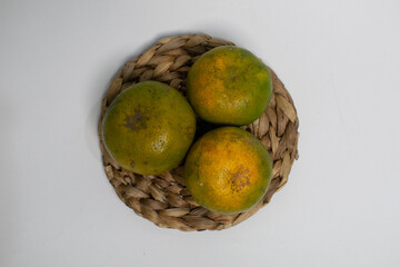 Organic oranges with natural blemishes are placed on a rustic straw mat.