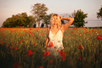 young beautiful blonde woman in white dress in poppy field at sunset. Woman and nature
