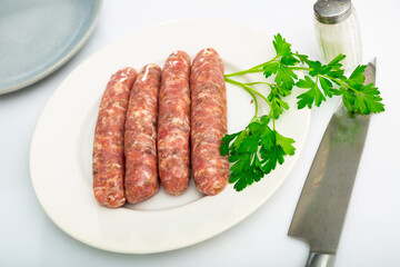Plate with raw popular Catalan sausages botifarra and fresh greens prepared for cooking on table...