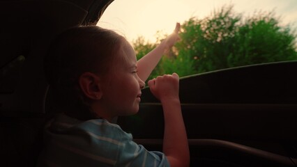 Girl child riding in car catches wind from auto window with hand. Family car trip. Girl sitting in...