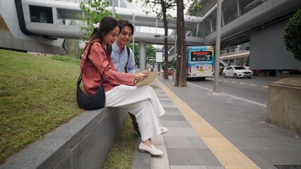 Two businesspeople sitting and consulting documents on a sidewalk in a modern city