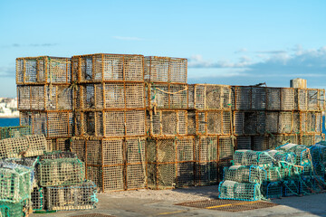 Large collection of crab traps is neatly stacked at a harbor dock. The sun is shining brightly, and the blue sky complements the scene while creating a vibrant atmosphere.