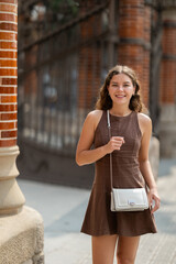 Young woman in a summer dress against the background of a brick wall and a metal fence. Woman...
