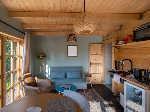 Modern tiny house interior with wooden ceiling beams, blue sofa, and compact kitchen with natural lighting