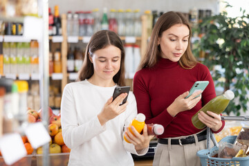 Positive teenage girl and her mother scanning QR on bottle of smoothie in grocery