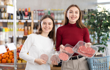 Happy teen girl and her mom deciding between beef burger and steak in supermarket