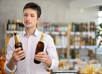 Adult man buyer chooses bottle of beer in grocery store..