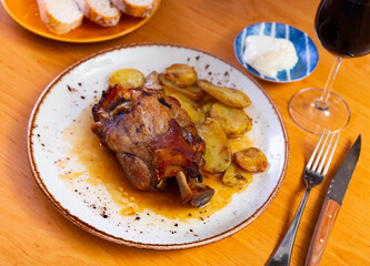 Portion of pork knuckle with boiled potatoes and gravy in white plate